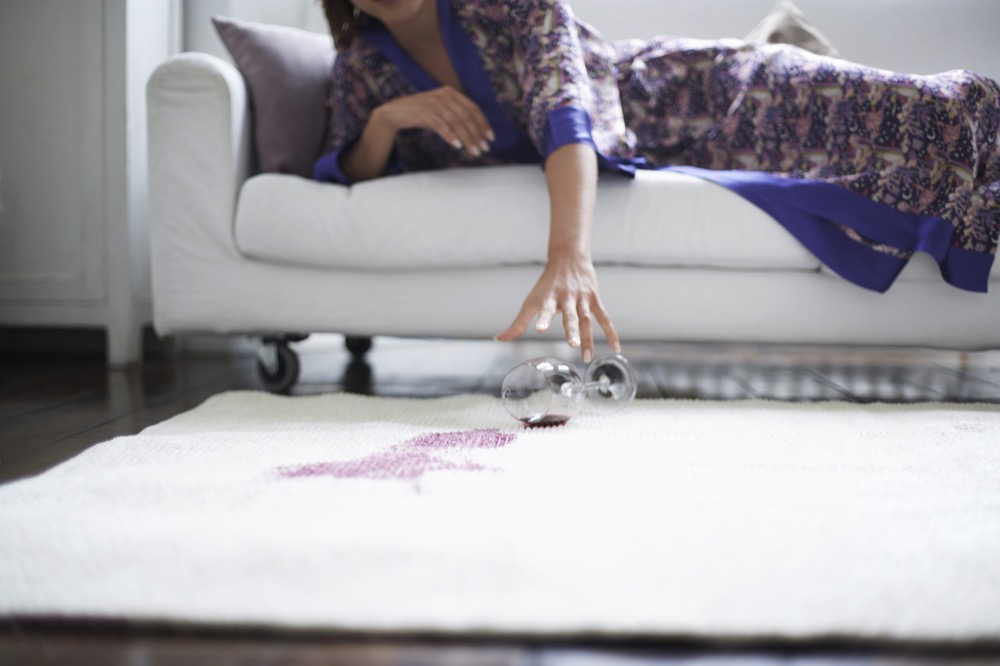 woman reaching toward spilled wine glass on rug